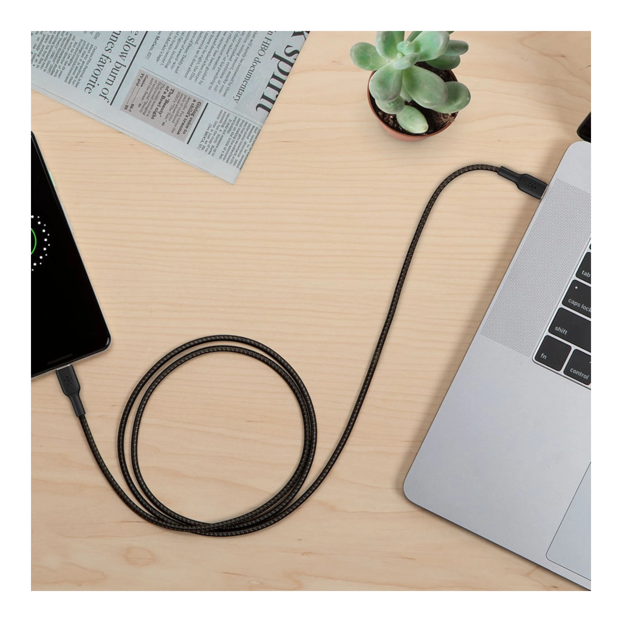 Cable USB-C a USB-C trenzado negro de doto.com.mx conectando un smartphone a un portátil sobre una mesa de madera.