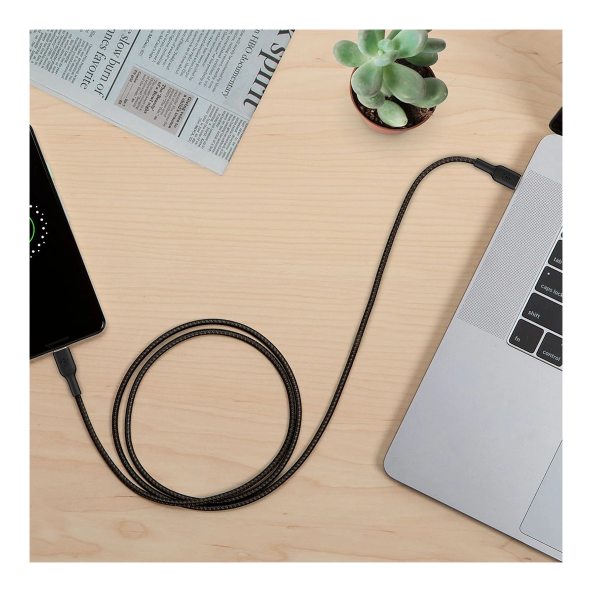Cable USB-C a USB-C trenzado negro de doto.com.mx conectando un smartphone a un portátil sobre una mesa de madera.